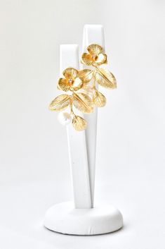 a pair of gold earrings with leaves on them sitting on top of a white stand