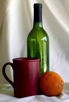 there is a green bottle and a red cup next to an orange on the table