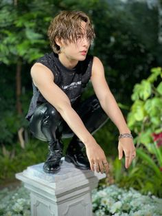 a young man sitting on top of a statue in the middle of a flower garden