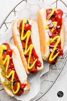 two hot dogs on buns with ketchup, mustard and relish sitting on a plate