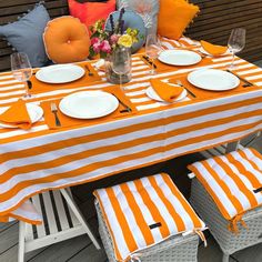 an orange and white striped table cloth with place settings on it, sitting on a deck