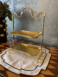 two tiered gold trays on top of a checkered tablecloth with a potted plant in the background