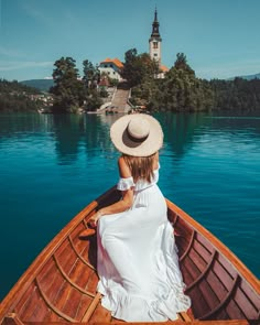 a woman in a white dress and straw hat sitting on a boat looking out over the water