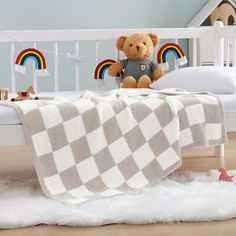 a teddy bear sitting on top of a bed with a checkered blanket over it