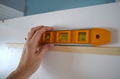 a hand is holding an orange and yellow light switch on a white wall next to a wooden rail