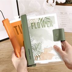 a person holding an open book on top of a wooden table next to other books