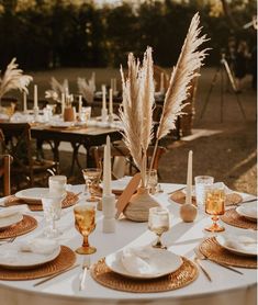 the table is set with plates, silverware and gold place settings for an outdoor dinner party