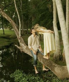 a man and woman are sitting on a tree branch in front of a pond with water