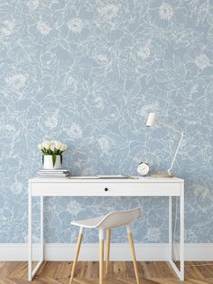 a white desk and chair in front of a blue wall with flowers on the wall