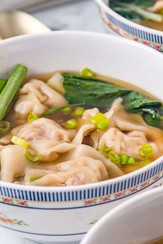 two bowls filled with dumplings and vegetables on top of a table