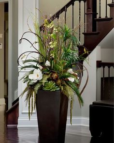 a tall planter with white flowers and greenery sits in front of a staircase