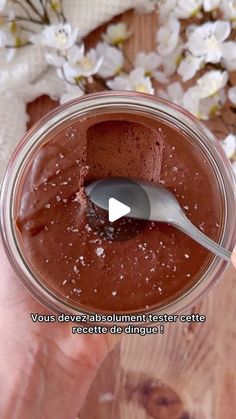 a person holding a spoon in a jar filled with chocolate pudding