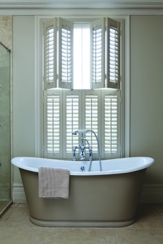 a bath tub sitting next to a window with shutters on the outside and inside