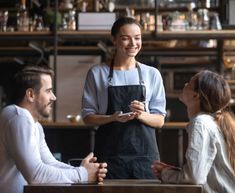 three people sitting at a table and one is holding a remote control in her hand