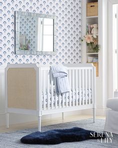 a white crib in front of a blue and white wallpaper