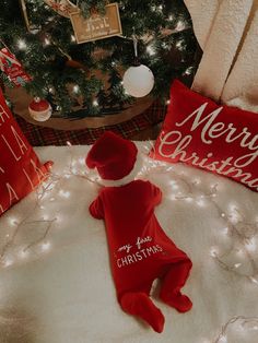 a red teddy bear laying on top of a white blanket next to a christmas tree