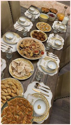 the table is set with many plates and silver wares on it, including pies