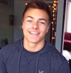 a young man is smiling and wearing a blue hoodie in front of a christmas tree