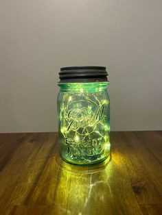 a green mason jar filled with lights on top of a wooden table