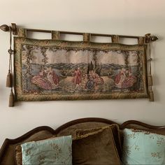 an old tapestry hanging on the wall above a bed with pillows and throw pillow cases