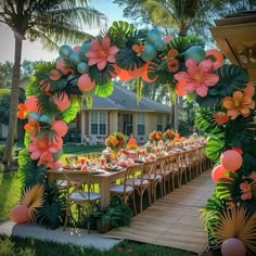 an outdoor table set up for a party with balloons and flowers on the arch over it