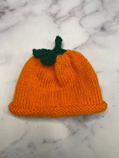 an orange knitted beanie with a green leaf on the top sitting on a marble surface