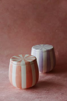 two ceramic containers sitting next to each other on a pink surface