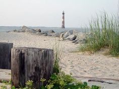 a light house sitting on top of a sandy beach next to grass and rocks in front of the ocean