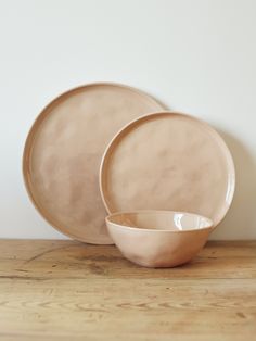 two plates and one bowl are sitting on a wooden table top in front of a white wall