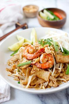 a white plate topped with noodles and shrimp next to chopsticks on a table