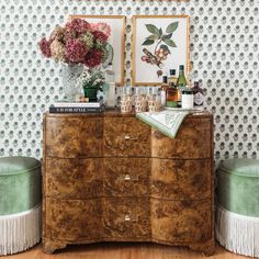 an old dresser with flowers and bottles on it in front of a wallpapered wall