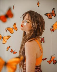 a woman with glasses looking at butterflies flying in the air over her head and body