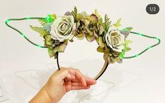 a hand holding a flower headband with green lights