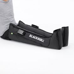 a blackroll bag sitting on the ground next to a person's leg and arm