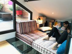 a woman sitting on top of a couch next to an open window reading a book