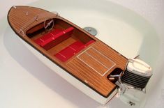 a small wooden boat with red seats in a bathtub