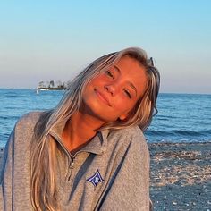 a woman is sitting on the beach with her head turned to the side and looking at the camera