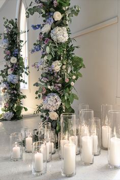 candles are lined up on a table with flowers and greenery