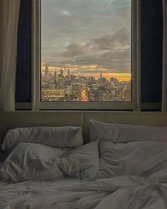 an unmade bed in front of a window overlooking the city