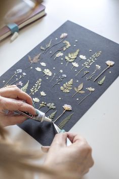 a woman is using scissors to cut out pressed flowers on a piece of black paper