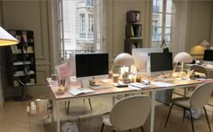 a desk with two computer monitors on it in front of a lamp and bookshelf