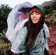 a woman wearing a raincoat and carrying a child in her arms on a rocky trail