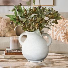 a white vase filled with green leaves on top of a table next to a book