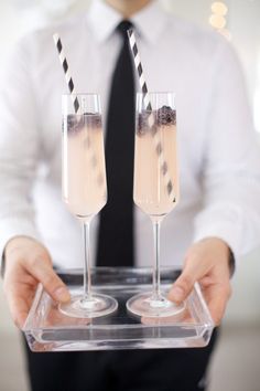 two glasses of champagne being held by a man in a white shirt and black tie