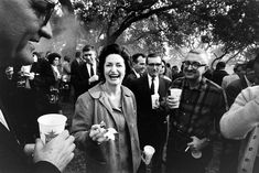 a group of people standing around each other with cups in their hands and one woman laughing