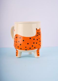 an orange and white ceramic cat mug on a blue surface with black dots around it