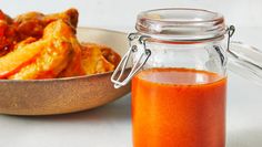 a glass jar filled with sauce next to a bowl of food