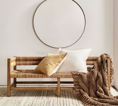 a wooden bench with two pillows and a round mirror on the wall above it in a white room