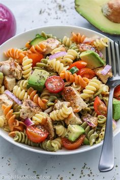 a white bowl filled with pasta salad next to an avocado and tomato slice