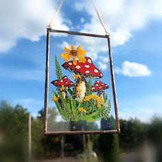 a photo hanging from a metal frame with flowers and mushrooms on it in front of a blue sky